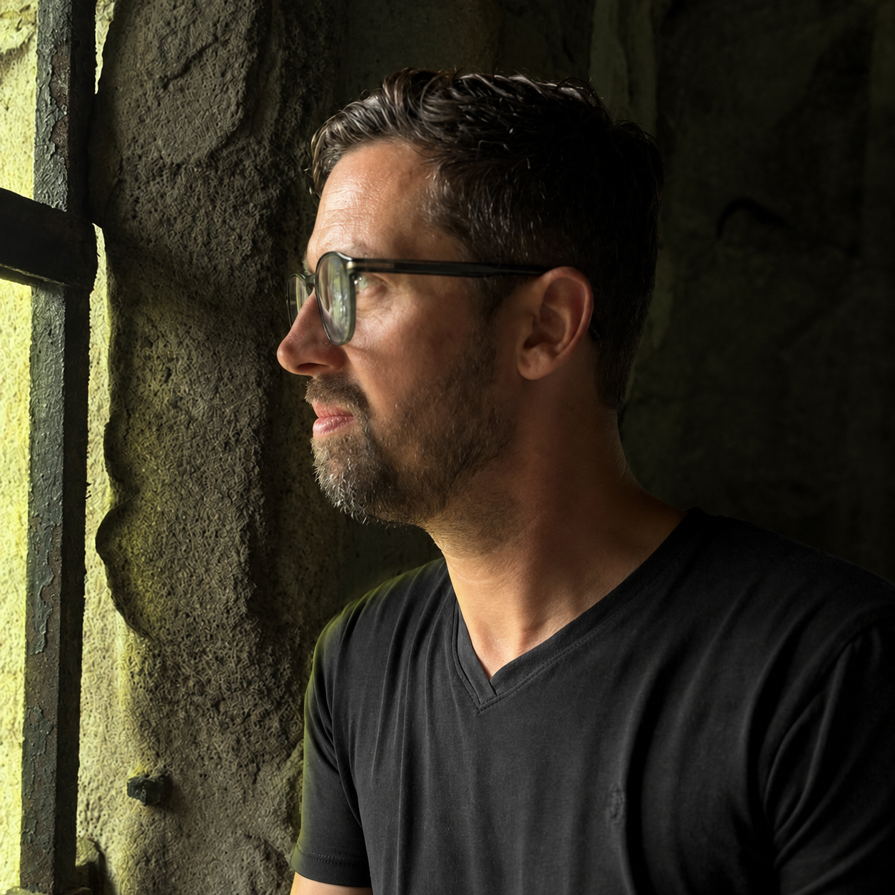 Organic Sequence looking toward the window, wearing glasses and a black shirt.